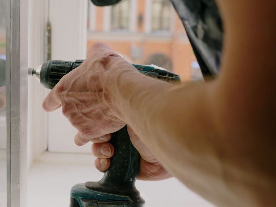 Hands fixing a window frame with a cordless screwdriver